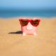 A piggy bank at the beach wearing sunglasses