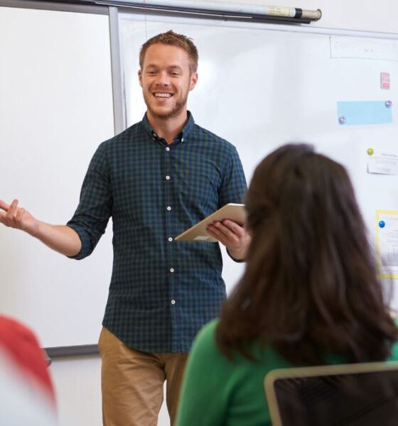 Male teacher smiling in front of the class students and explaining
