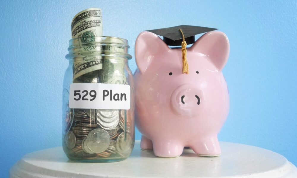 A pink piggy bank wearing a graduation cap next to a money jar with 529 plan text on it
