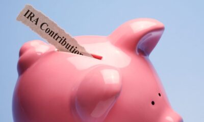 A slip of paper that says IRA contribution being inserted into a pink piggy bank